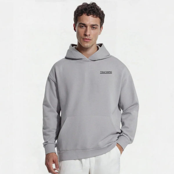 Homme portant un hoodie gris clair TOURISMO avec un pantalon blanc sur fond neutre