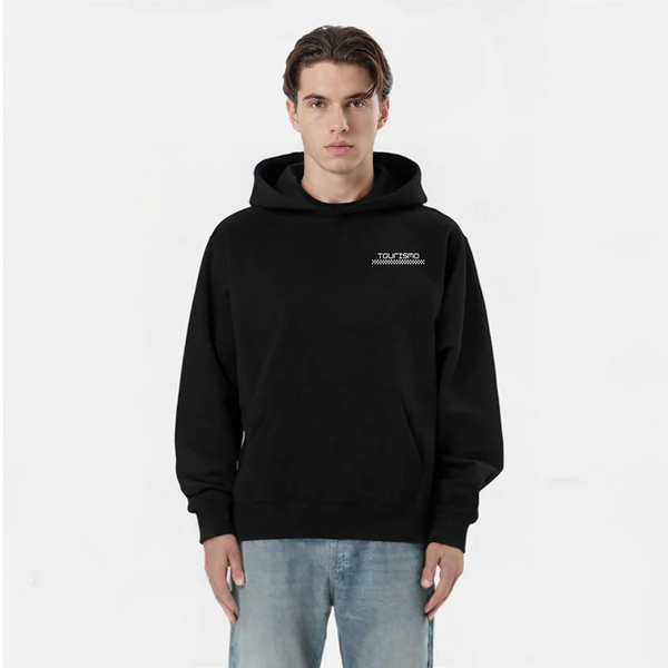 Homme portant un hoodie noir TOURISMO avec un jean clair, sur fond blanc